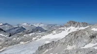 A high-altitude panorama with rocky peaks and small glaciers as far as the eye can see, all under a bright blue sky